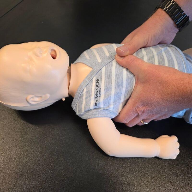 Infant CPR training manikin on a table with an adult delivering chest compressions.