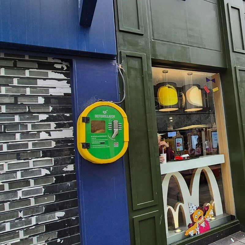 Public defibrillator mounted on a blue wall beside a McDonald's storefront window.
